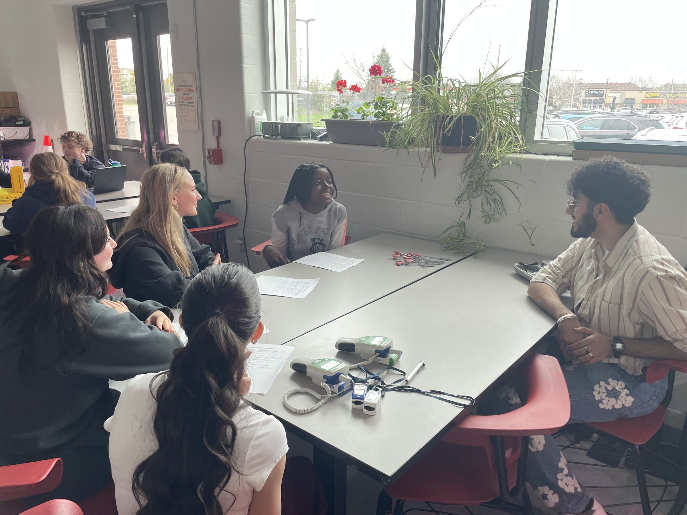 Students seated around a table with thermometers and pulse oximeters, chatting with a mentor