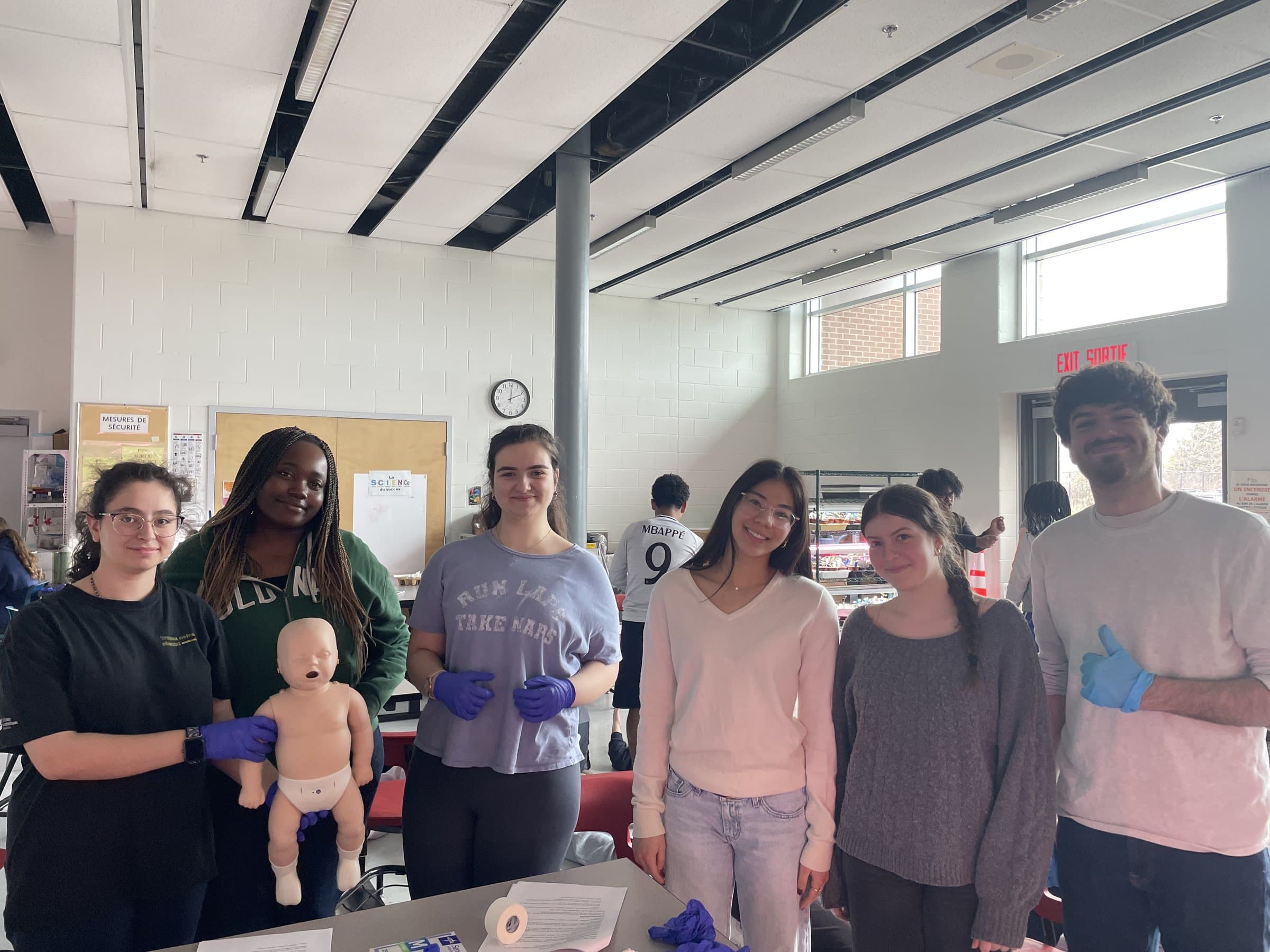 Students and a mentor pose with an infant CPR mannequin