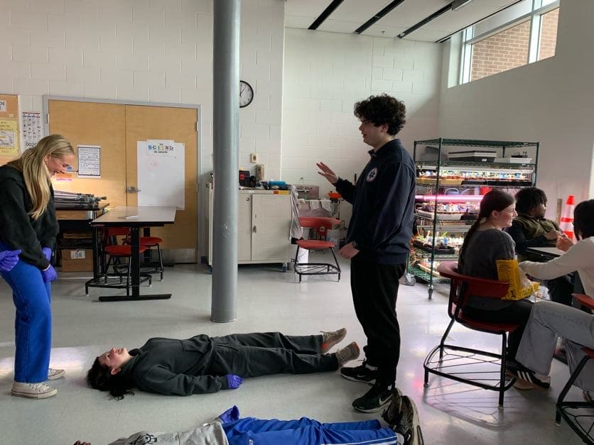 A student responder assesses the scene as volunteers lie on the floor acting as patients